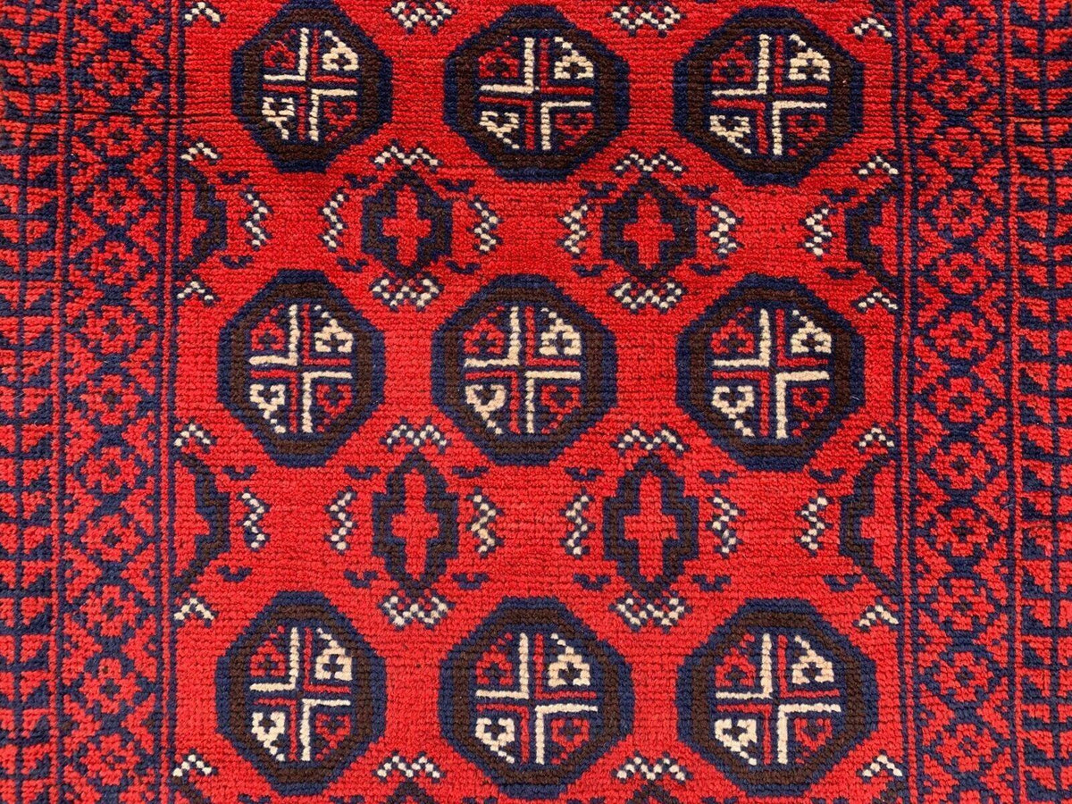 Close-up of a hand-knotted Afghani wool Baluch runner rug featuring red background with black and white geometric octagonal motifs and intricate border patterns.