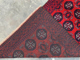 Corner view of a hand-knotted Afghani wool Baluch runner rug featuring dark red and black geometric octagonal motifs with white accents on a textured light gray floor.