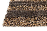 Close-up of a handwoven shag rug with alternating dense and sparse bands in shades of brown, black, and tan creating a striped, textured pattern.