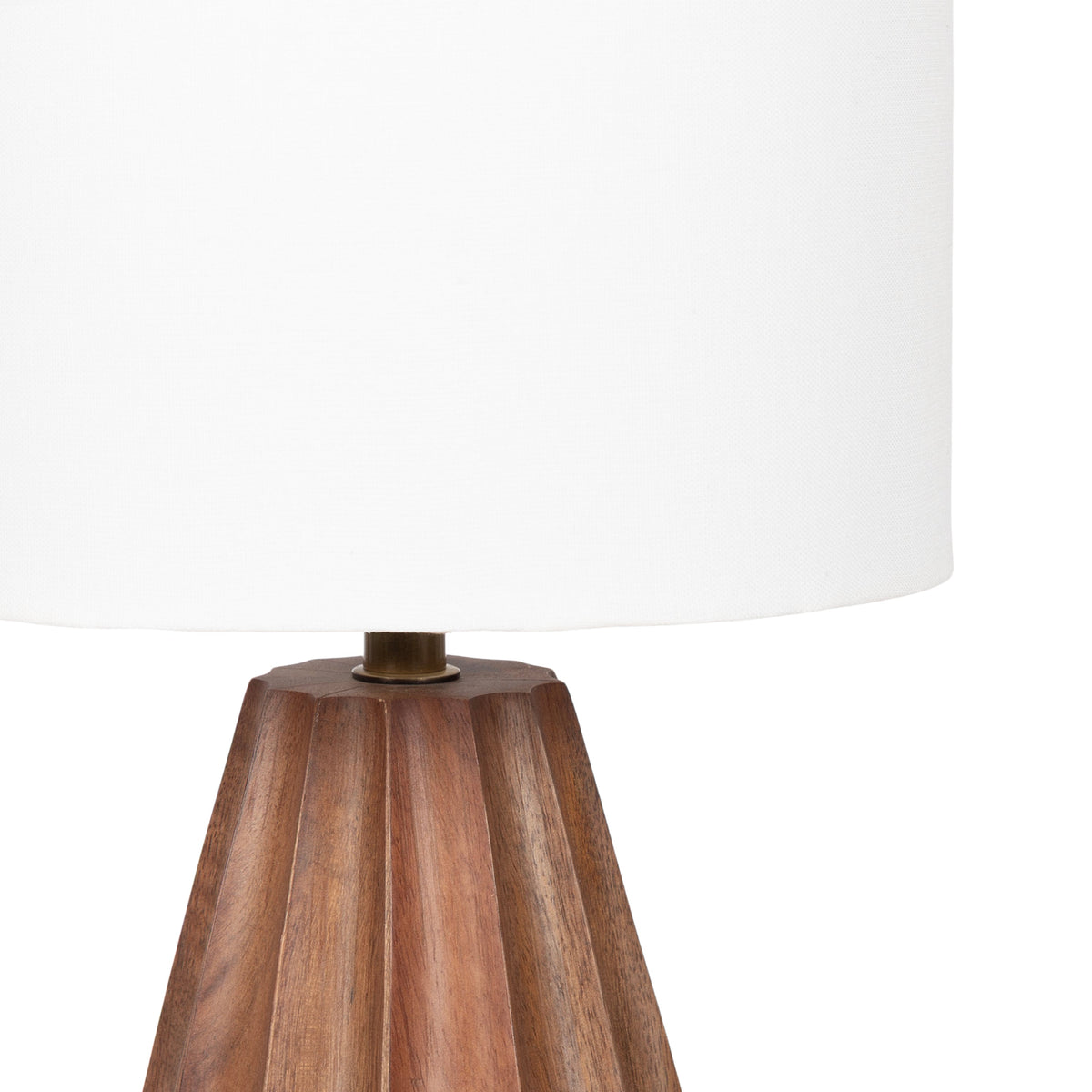 Table lamp with a scalloped, faceted wooden base in warm brown tones topped by a large, white cylindrical fabric lampshade.