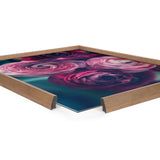 Close-up angled view of a framed printed art piece featuring detailed pink and purple ranunculus flowers with a teal background inside a light wooden frame.