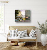 Canvas print of a street scene with a yellow taxi, buildings, and a pedestrian, hung above a wooden bench with plaid cushions in a bright room.