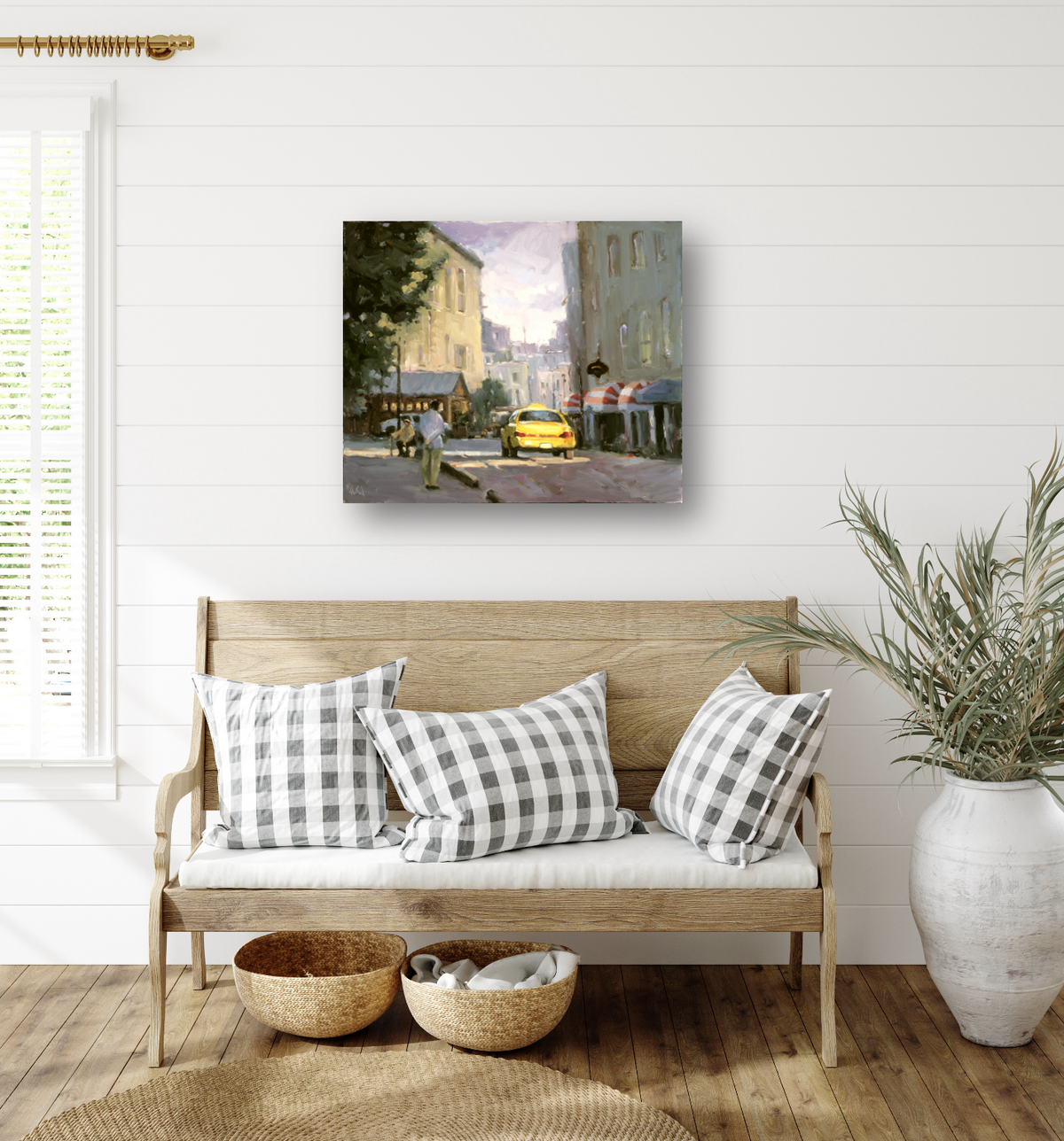 Canvas print of a street scene with a yellow taxi, buildings, and a pedestrian, hung above a wooden bench with plaid cushions in a bright room.