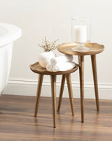 Two bronze metal plant stands with irregular scalloped tops, shown with a glass candle holder and a small white vase with dried flowers and rolled towels.
