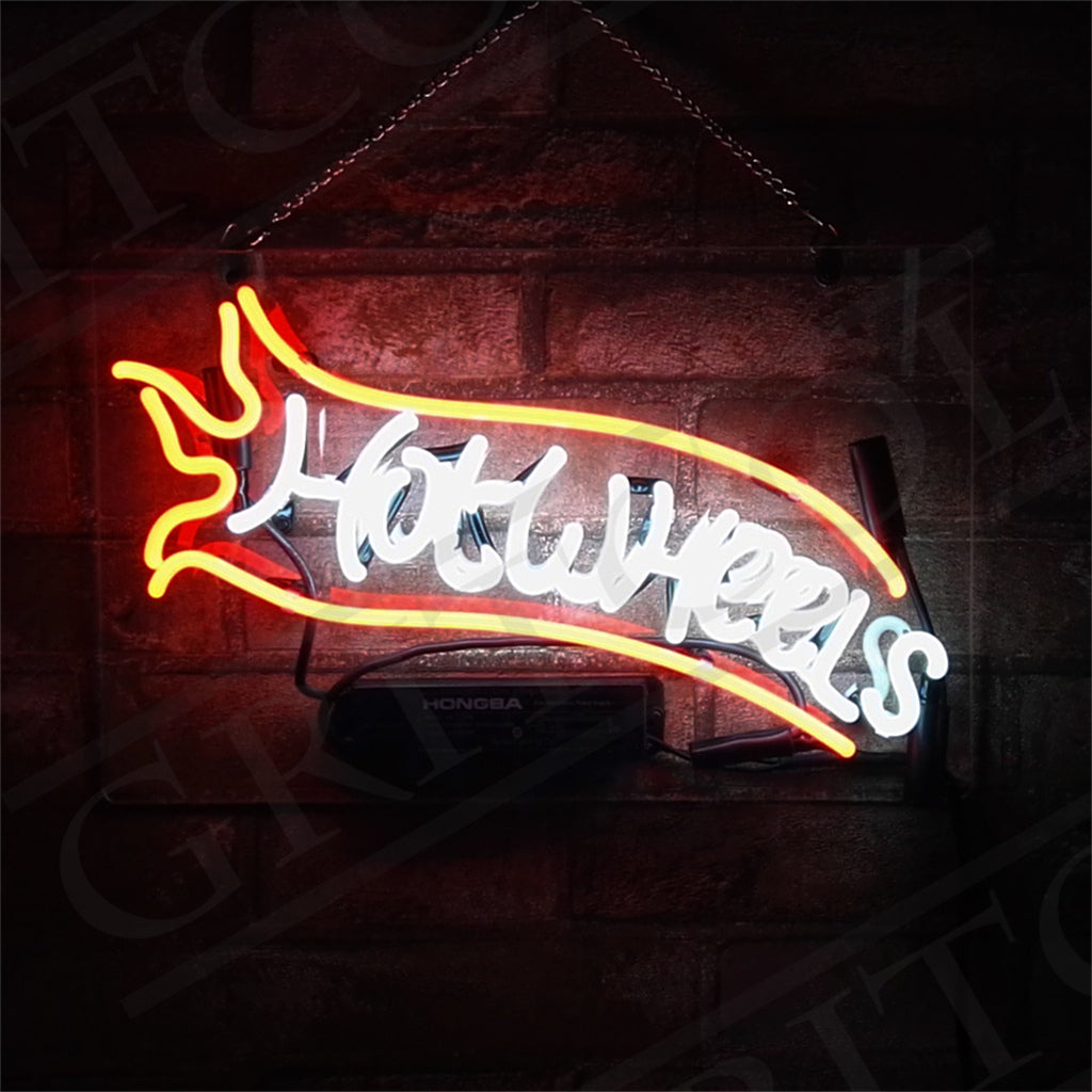 Rectangular neon sign featuring the word 'Hot Wheels' in white with an orange flame design extending from the left side against a brick wall background.