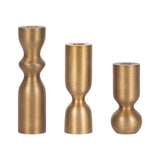 Set of three gold-colored taper candle holders in varying curvy cylindrical shapes, arranged in descending height from left to right against white background.