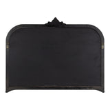 Black arched wall mirror frame with rounded corners and decorative floral crest at the center top, featuring slightly worn metal surface and hanging hardware on sides.