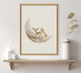 Framed canvas depicting a fawn and a rabbit resting together on a large beige crescent moon, surrounded by small white stars on a light background.