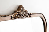Arched wall mirror with a carved wooden frame featuring a central floral motif and a beaded edge detail in a warm brown finish.