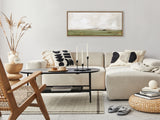 Neutral-toned living room with beige sectional sofa and black oval coffee table, decorated with black-and-white patterned pillows and minimalist landscape canvas above.