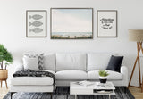 Living room with white sectional sofa, patterned gray and black pillows, black and white rug, and three framed artworks: fish print, seascape, and adventure quote.