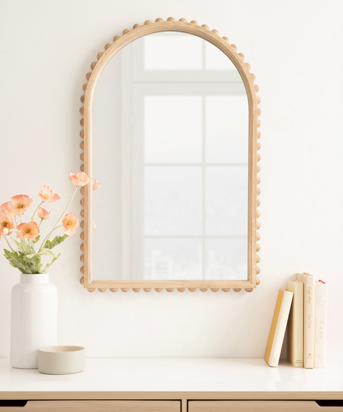 Arched wall mirror with natural wood frame featuring evenly spaced rounded beads along the edge, reflecting a soft-lit window grid.