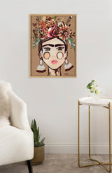 Framed canvas painting of a stylized portrait of a woman with bold eyebrows, large earrings, and a vibrant floral crown in warm earthy tones hanging on a white wall.