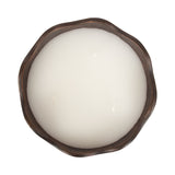 Top view of a round white three-wick candle in a brown metal bowl with an irregular, wavy edge.