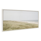 Framed canvas showing a muted coastal landscape with soft green dune grasses in the foreground and a calm sandy beach meeting a gentle gray-blue ocean under an overcast sky.