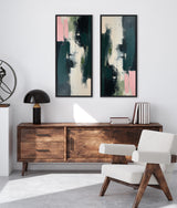 Two vertical abstract paintings with dark green, cream, and blush pink brushstrokes in black frames hung side by side above a mid-century wooden console and white armchair.