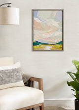 Abstract landscape painting with soft pastel-colored sky and layered green hills, framed and hanging on a beige wall above a cream armchair and near a green plant.