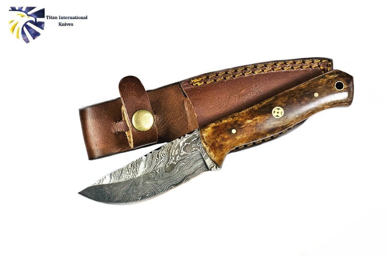 Custom hand-forged Damascus steel hunting knife with burnt bone handle and leather sheath.