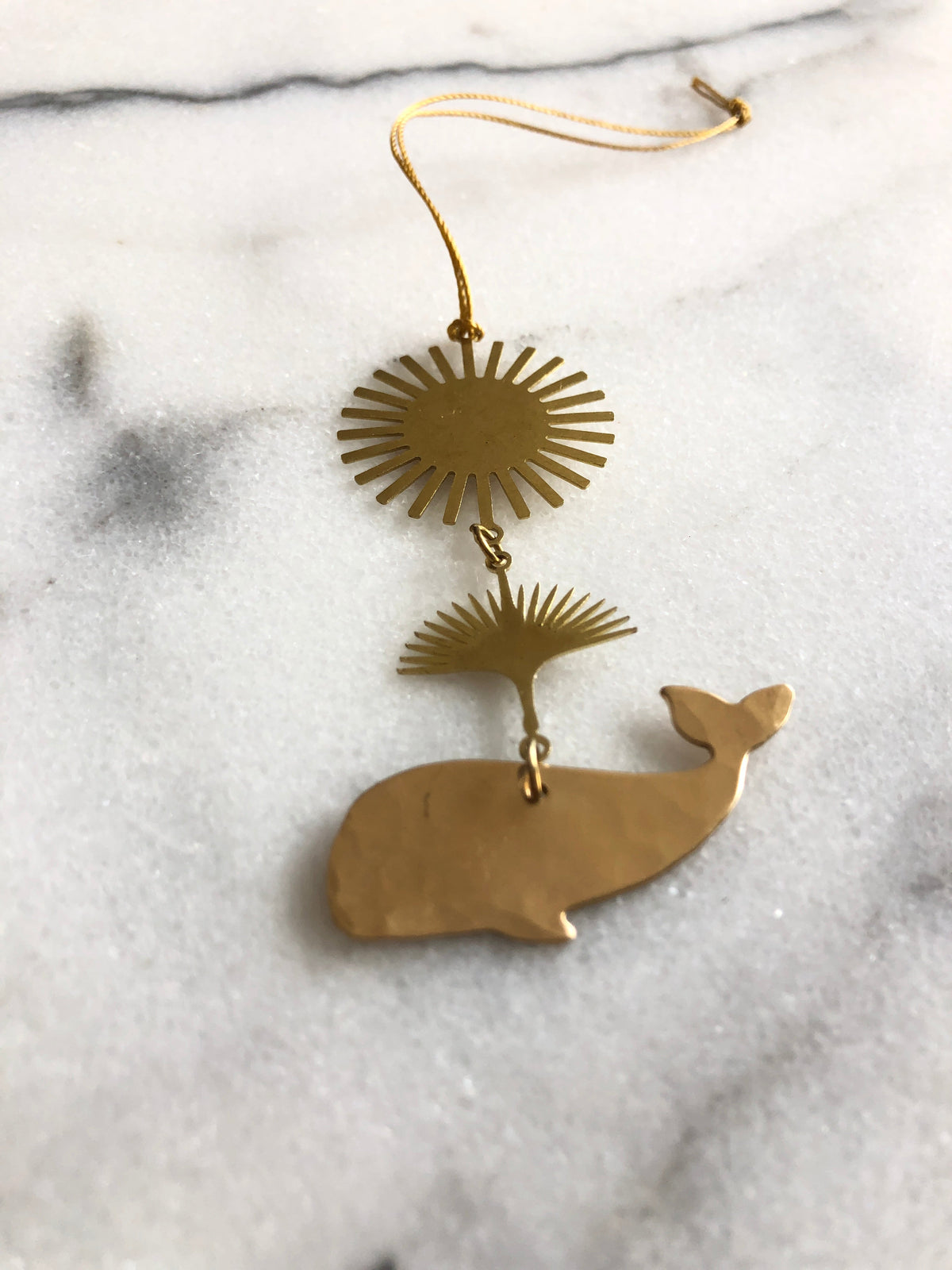 Gold-colored metal ornament featuring a stylized sun at the top, a whale spouting water in the middle, and a whale figure at the bottom, connected by small rings.