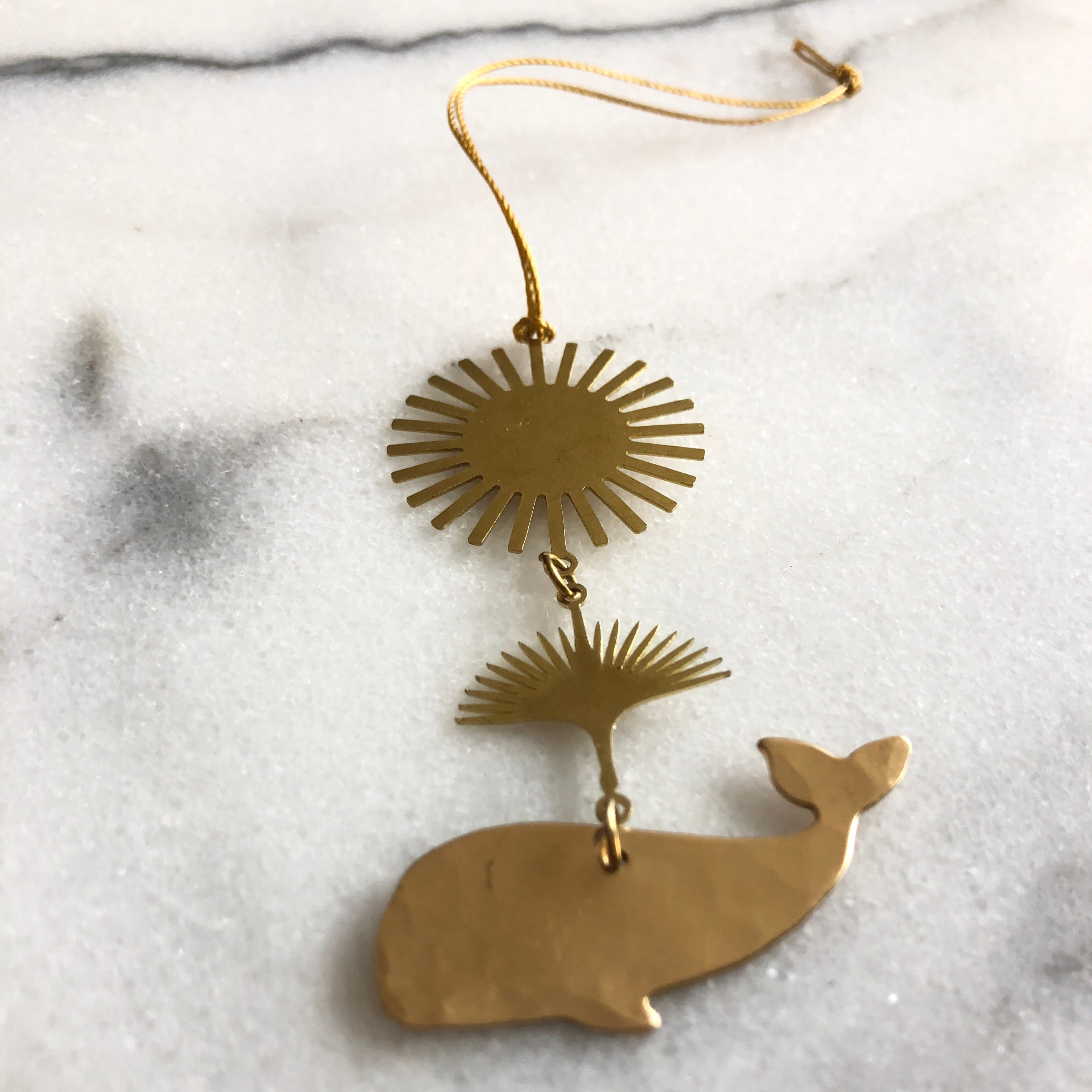 Salish Whale Ornament by Vida + Luz, hand-cut hammered brass whale silhouette with hanging cord, displayed against white background