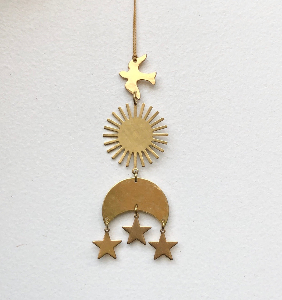 Brass hanging ornament with a bird at the top, a sunburst in the middle, and a crescent moon with three dangling stars at the bottom against a white background.