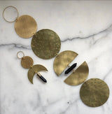 Brass circular and crescent moon-shaped pendant with black quartz crystal accents connected by small rings on a white marble background.