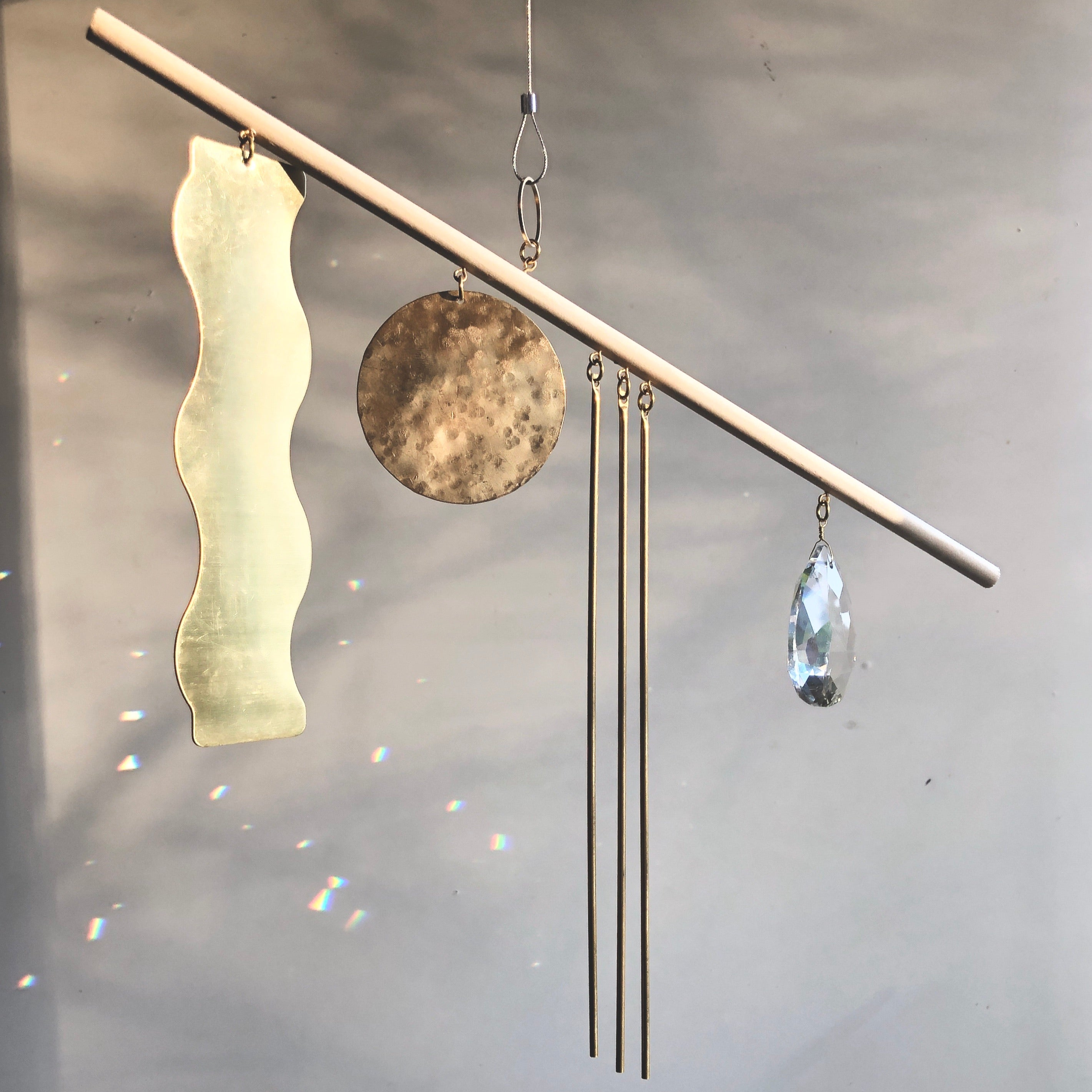 Goldy Suncatcher wall hanging showing hand-cut hammered brass, vintage glass crystal, and raw wood elements
