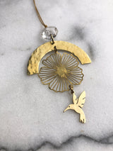 Gold-toned ornament featuring a hammered crescent arch, delicate wireframe flower, and a small hummingbird charm suspended below, with a vintage clear glass crystal bead at the top.