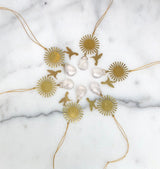 Circular gold sunburst ornaments paired with small gold hummingbird shapes and teardrop-shaped clear rose quartz stones, arranged in a circle on white marble.