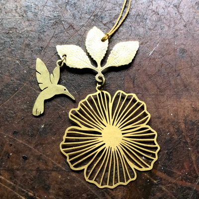 Hibiscus Hummingbird Ornament made of hammered brass hanging against a neutral backdrop