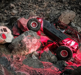 Red off-road vehicle climbing over large rocks with red LED lights illuminating the rocky terrain below it at night