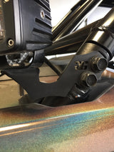 Close-up of black metal pillar mount with bolts securing a device on a vehicle frame with iridescent paint shifting green and purple hues.