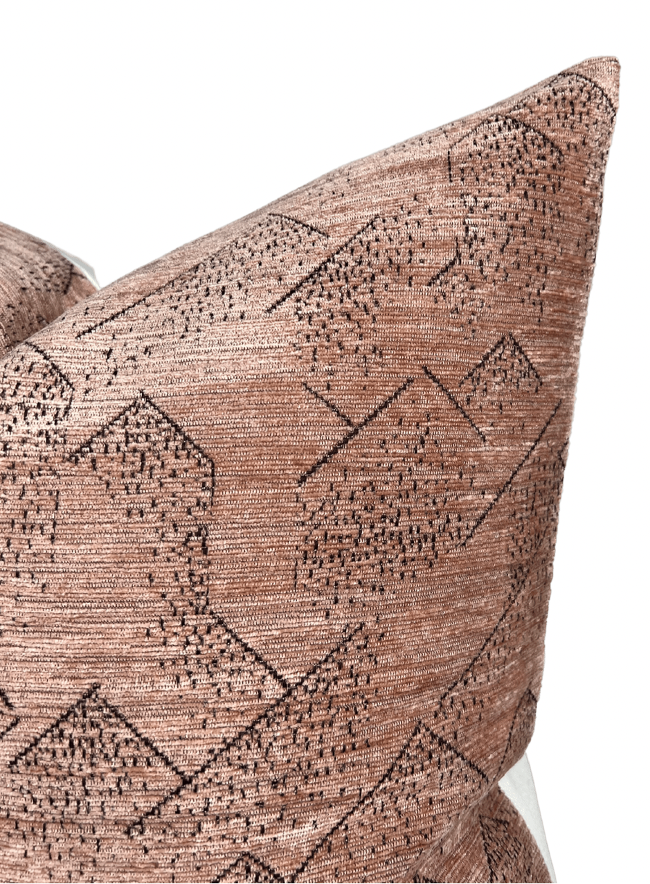 Close-up of a rose-colored pillow cover featuring a textured woven pattern of black geometric shapes and diagonal lines.