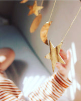 Close-up of gold hammered brass ornaments in star, crescent moon, and circular shapes hanging from strings against a softly lit background with a striped sleeve reaching towards them
