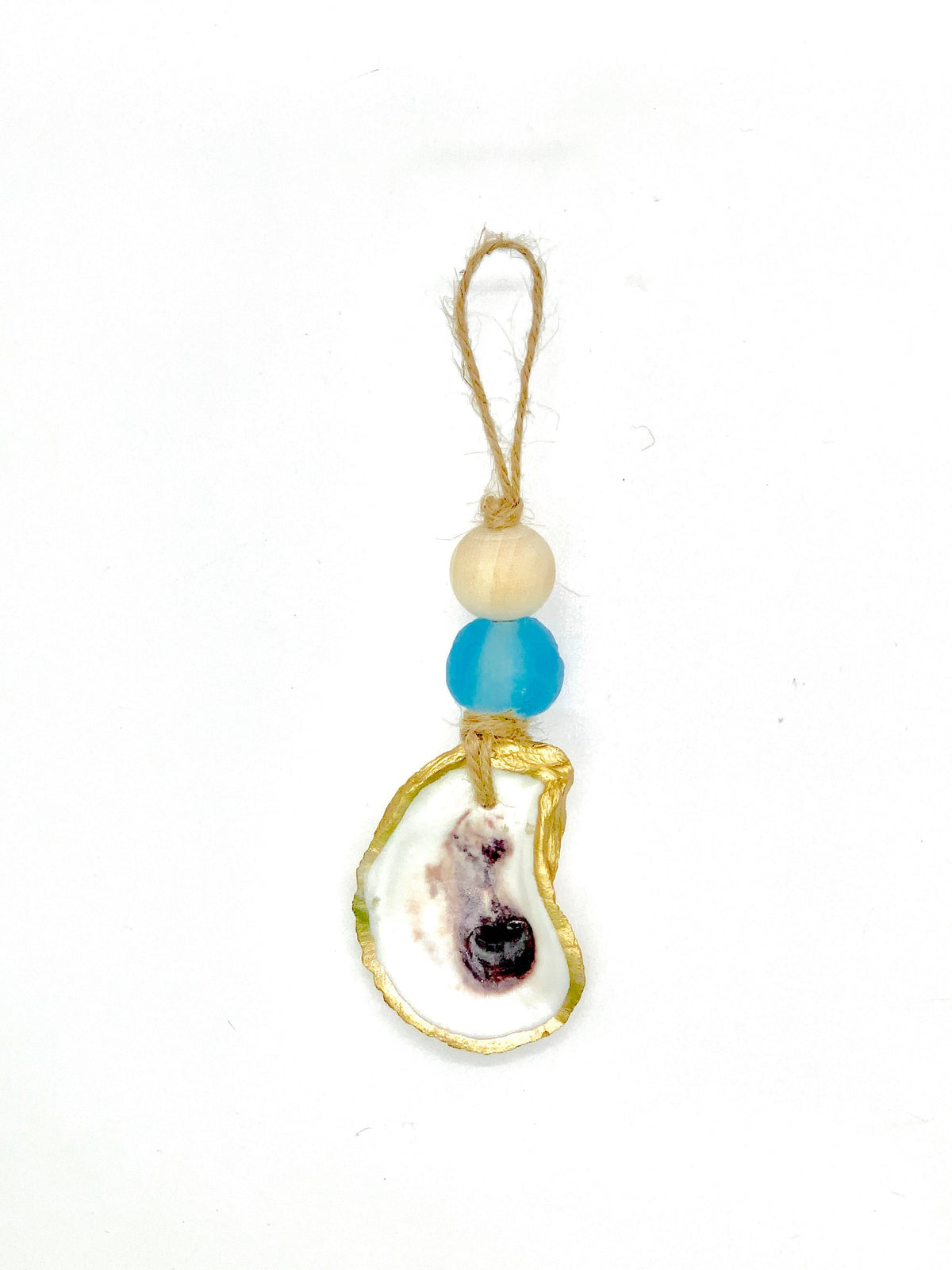 Ornament with a natural shell piece edged in gold, hanging below a beige round bead and a blue frosted sea glass bead, all attached to a twine loop.