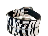 White and black tiger-print hair-on-hide leather pet collar with silver-toned buckle and rivet hardware, shown in close-up at an angle.