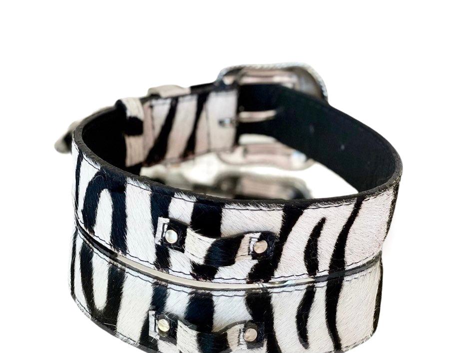 White and black tiger-print hair-on-hide leather pet collar with silver-toned buckle and rivet hardware, shown in close-up at an angle.