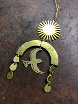 Hammered gold-tone metal ornament featuring a sunburst at the top, a curved arch with a flying bird silhouette in the center, and three teardrop dangles on each side.
