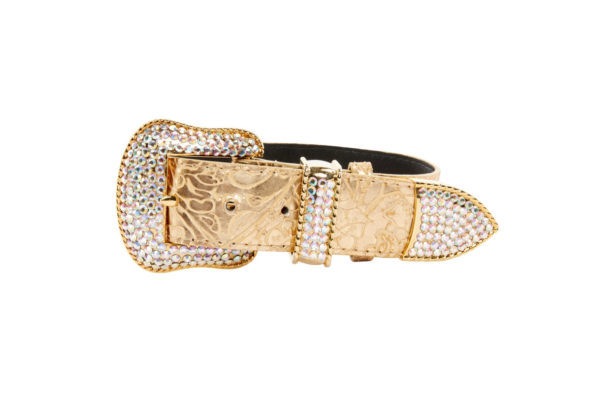 Gold floral-patterned leather belt with a large buckle and tip adorned with multicolored Swarovski crystals, shown coiled against a white background.