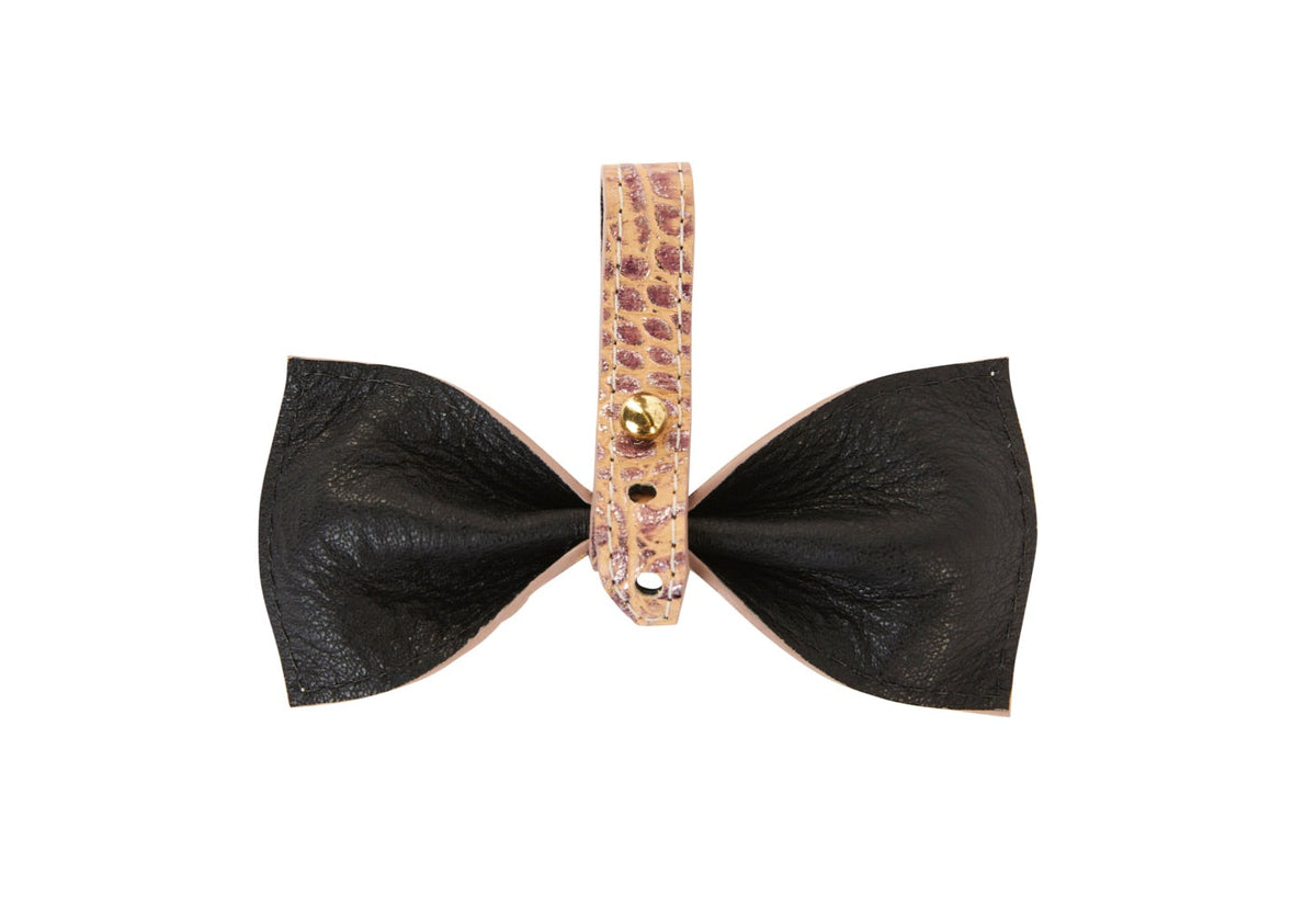 Bow-shaped object with black textured leather petals and a central strap in pink embossed croc pattern secured by a small gold button.