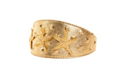 Gold-tone leather cuff with embossed starfish and pyramid stud details along the surface, shown at a slight angle on white background.