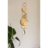 Hanging suncatcher with five brushed gold geometric shapes—circles and semi-circles—connected vertically, topped by a hanging ring and ending with a clear teardrop crystal at the bottom.