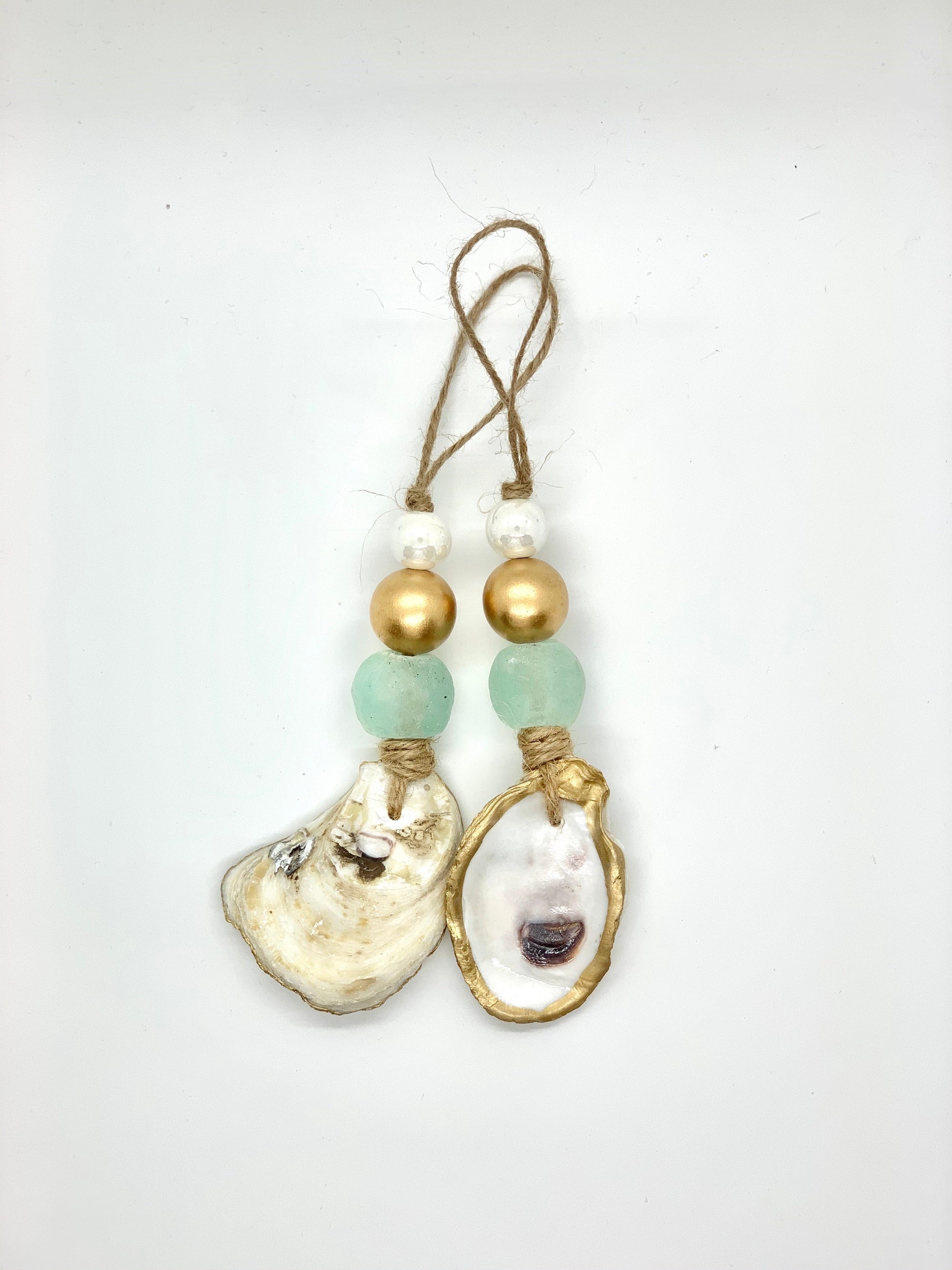 Two gold gilded oyster shell ornaments with sea glass beads hung on a tree branch