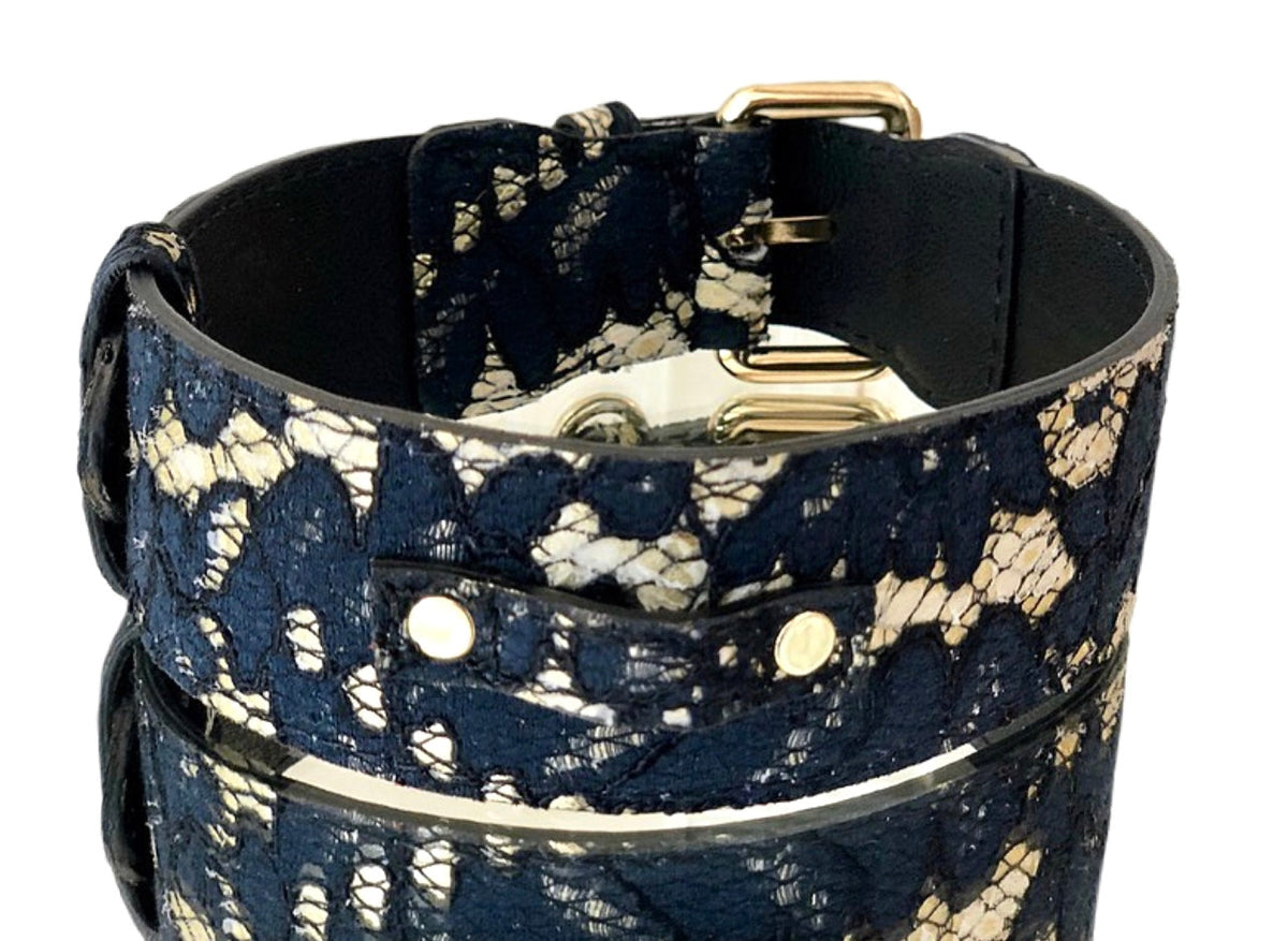 Close-up of a navy lace fabric layered over beige leather pet collar with gold metal buckle and rivets, highlighting texture and classic contrast.