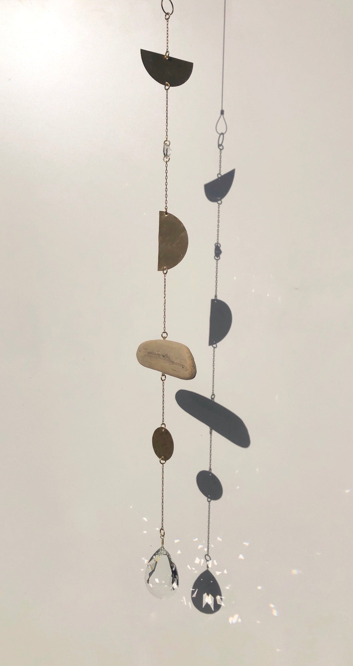 Two vertical hanging chains with mixed geometric metal shapes and natural stone pieces, ending in faceted clear crystal pendants that catch light.