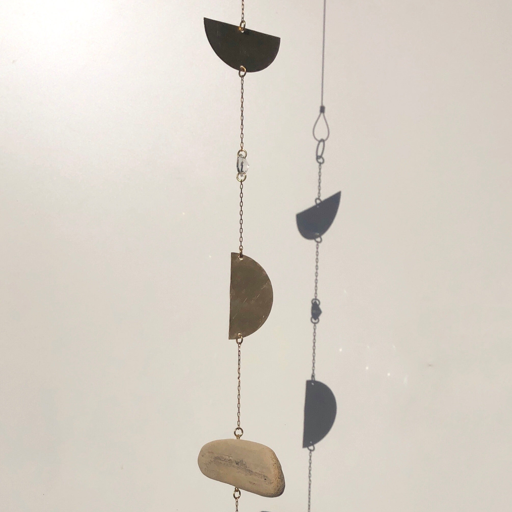 Rapture Suncatcher by Vida + Luz made of hand-hammered brass, vintage crystals, and driftwood hanging on a wall