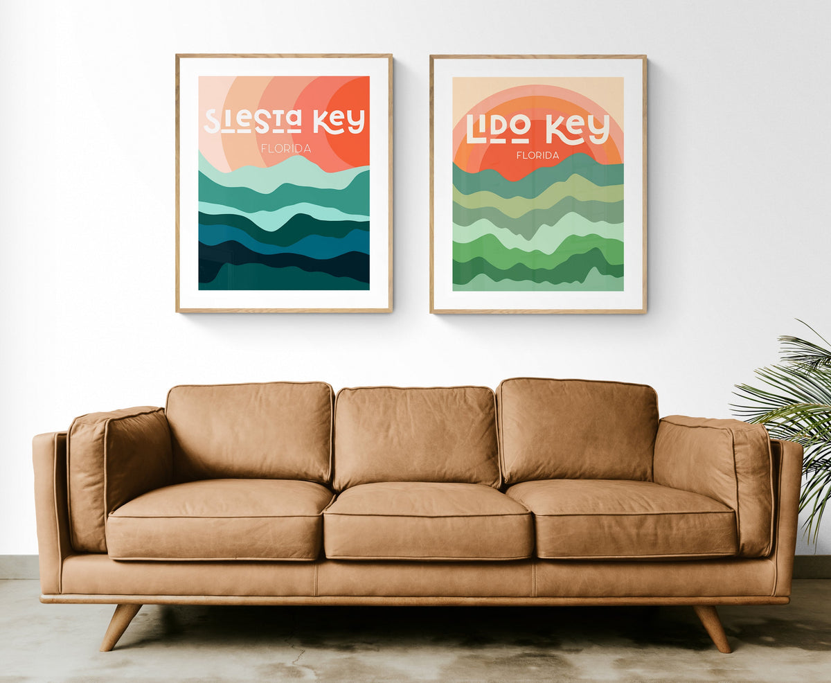 Two framed modern art prints above a tan leather sofa, each with layered wavy shapes in green and blue hues and the text 'Siesta Key Florida' and 'Lido Key Florida' on orange backgrounds.