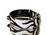 Zebra print hair-on-hide rectangular dog collar with silver buckle hardware and embossed 'Allysa Payne Beverly Hills' branding inside, shown on reflective surface.