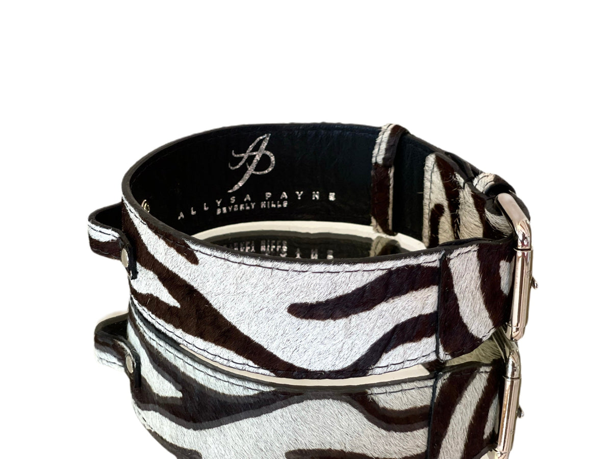 Zebra print hair-on-hide rectangular dog collar with silver buckle hardware and embossed 'Allysa Payne Beverly Hills' branding inside, shown on reflective surface.