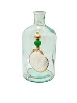 Clear glass bottle with a rounded shoulder holding a string tied to a white scallop shell accented with one gold and one green wooden bead.